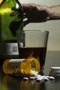 Hand reaching for wine and prescription pills on table, vertical