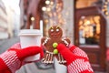 Hand in red mitten holding coffee cup and a smiling gingerbread man. Christmas mood in blurred background. Christmas Royalty Free Stock Photo