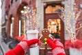 Hand in red mitten holding coffee cup and a smiling gingerbread man. Christmas mood in blurred background. Christmas Royalty Free Stock Photo