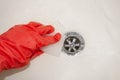 A hand in a red rubber glove with a melamine sponge rubs the white bathroom near the drain hole where the water flows