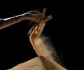 Hand releasing dropping sand on hill. Fine Sand flowing pouring through fingers hand against black background. Summer sand hill