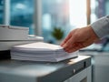 Hand removing printed pages from a copier machine in a modern office with a blurred background of natural light and workspace Royalty Free Stock Photo