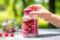 a hand removing a raspberry macaron from a glass jar