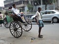 A hand rickshaw puller pulls a man in the middle of the road.