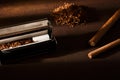 Hand-rolled cigarette, rolling machine, cigarillos, scattered tobacco on background, cigarette roll with filter, cigarette filters Royalty Free Stock Photo