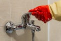 Hand in rubber glove cleans dirty calcified shower mixer tap, close up