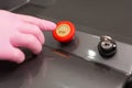 A hand in rubber gloves presses the red button of the laser device. Close-up