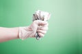 hand in a rubber white medical disposable glove clenches wrinkled dollar bills in a fist on a green background Royalty Free Stock Photo