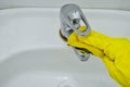 Hand in a rubber yellow glove washes the faucet on the sink with a sponge Royalty Free Stock Photo