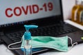 Hand sanitizer bottle and surgical mask on a laptop keyboard that reads covid-19 on the screen. Illustration to protect office