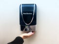 Hand sanitizer dispenser with hand underneath with sanitizing foam in palm