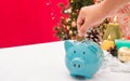 Hand saving money into piggy bank decorated in Christmas celebration theme on white table reb background with copy-space, family Royalty Free Stock Photo