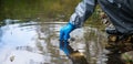 Hand scientist, in a protective suit and gloves, collects water in a glass tube for testing