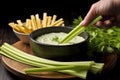 hand scooping cheese dip with a celery stick from a bowl