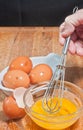 Hand scrambling egg in glass bowel with whisk, egg shells