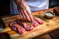 hand seasoning raw steaks on a wooden board before grilling