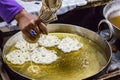 Hand seen pouring pastry into hot oil for a pretzel-like snack