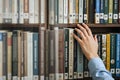 Hand Selecting a Book from a Full Bookshelf in a Library or Bookstore Setting with a Focus on Literature Royalty Free Stock Photo