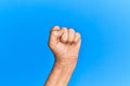 Hand of senior hispanic man over blue isolated background doing protest and revolution gesture, fist expressing force and power