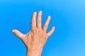 Hand of senior hispanic man over blue isolated background greeting doing vulcan salute, showing back of the hand and fingers, Royalty Free Stock Photo