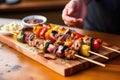 hand serving grilled kebabs on a wooden board