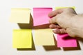 A hand shoots multi-Colored square post-it notes pasted on a white wall