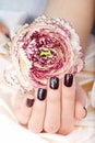 Hand with short manicured nails colored with dark purple nail polish and flower Royalty Free Stock Photo