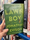 Hand showing a copy of the book Lawn Boy by Jonathan Davis from the library shelf