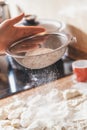 Hand sifts flour through sieve over dough pieces Royalty Free Stock Photo