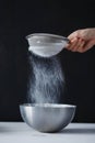 Hand sifts the powdered sugar and flour in an iron bowl on a black background on white wooden table close-up Royalty Free Stock Photo
