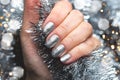 Hand With Silver Glittered Nails On Christmas Tinsel Background With Blurred Lights Bokeh