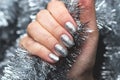 Hand With Silver Glittered Nails On Christmas Tinsel Background