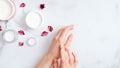 Hand skin care concept. Top view female hands applying organic moisturizing hand cream, jars with cosmetic cream and pink petal on