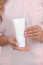 Hand skin care. Female hands holding one white cream tube against body in pink cloth, beautiful beautician woman hands with Royalty Free Stock Photo