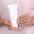Hand skin care. Female hands holding one white cream tube against body in pink cloth, beautiful beautician woman hands with Royalty Free Stock Photo