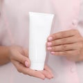 Hand skin care. Female hands holding one white cream tube against body in pink cloth, beautiful beautician woman hands with