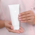 Hand skin care. Female hands holding one white cream tube against body in pink cloth, beautiful beautician woman hands with