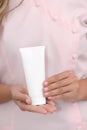 Hand skin care. Female hands holding one white cream tube against body in pink cloth, beautiful beautician woman hands with Royalty Free Stock Photo