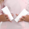 Hand skin care. Female hands holding two white cream tubes against body in pink cloth, beautiful beautician woman hands with Royalty Free Stock Photo