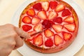 Hand slicing the best homemade strawberry tart. Isolated on wooden background.