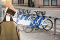 Hand with a smartphone and a backpack in front of a row of rental bikes.