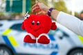 Hand with a soft toy in the shape of a heart on a defocused background of a police car Royalty Free Stock Photo