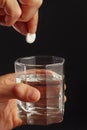 Hand with a soluble tablet from ache over the glass of water on black background. Royalty Free Stock Photo