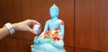 Hand splashing or pouring water to light green or blue Buddha statue with petal red rose, Jasmine