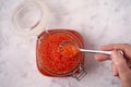 Hand with a spoon with red caviar over a glass jar filled with red caviar of salmon fish on a light background. Seafood, caviar Royalty Free Stock Photo