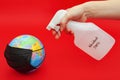 Hand spraying 70% alcohol on terrestrial globe model with black surgical mask isolated on red background. Royalty Free Stock Photo