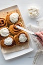 A hand spreading frosting on freshly baked cinnamon buns.