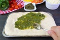 Hand spreading pesto sauce on the pizza dough before baking