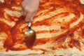 Hand spreading tomato sauce with a spoon