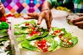 A hand sprinkling pan masala garnish and cherry on betel leaf during preparation of banarasi pan.